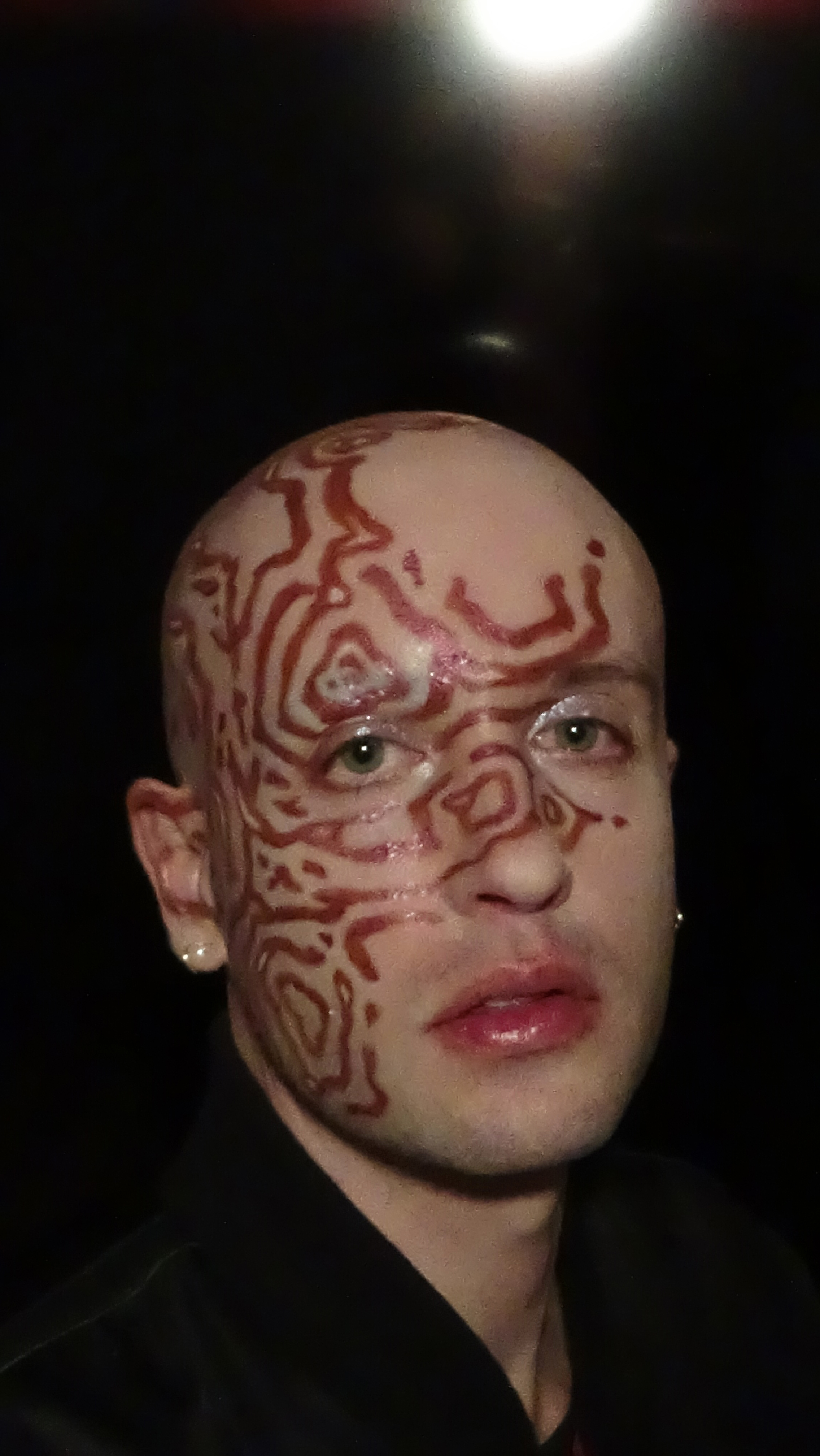 Close up portrait looking at the camera of Jesse with swirling maroon pattern makeup against a black background